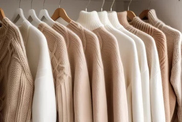 Tuinposter Beige white cashmere wool sweaters hanging in the closet. Cozy autumn and winter wardrobe, warm knitted dress close-up, retail clothing background. © svf74