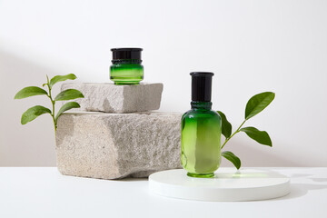 Set of cosmetic bottles for skin care placed on podium and gray block of stone with green tea leaves on white background. Space for design, advertising and branding cosmetic product