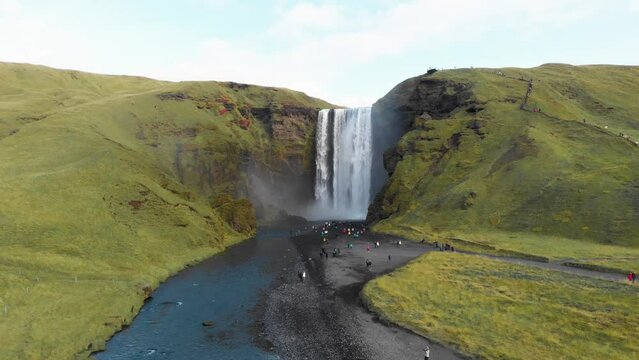 Tourist crowd on river shore visting Skogafoss waterfall in Iceland.