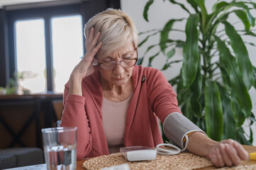 Older woman sitting alone at home, measuring her blood pressure with a home device