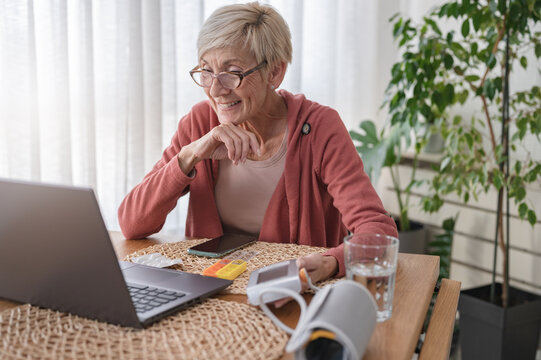 An elderly woman sitting in front of a laptop computer at home, having an online video call with a doctor. Online medical consultations. Telemedicin and telehealth - Powered by Adobe