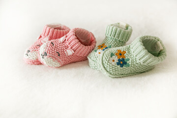 Pink and green knitted children's shoes on a white background with copy space. Pregnancy and motherhood concept, first birthday banner, handmade socks, baby warm clothes, handmade knitted socks