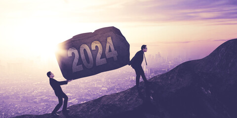 Two young businessmen lifting a stone with 2024 number while climbing on the cliff