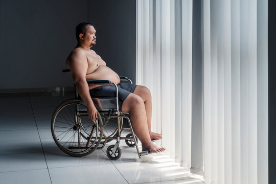 Picture of disabled fat woman looks pensive while sitting in the wheelchair by the window