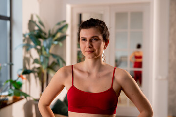 Fototapeta na wymiar Indoor shot of pretty girl in sport tank top standing with hands on hips. Inspired young woman in sporty outfit on blurred background
