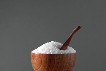 White table salt granules falling into a pile. Wood bowl. Gray color studio background. Condiment particles dropping. Clean cosmetic bath salt pouring footage. Closeup of grained sea salt pieces hill