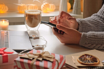 Woman using laptop and cell phone, making online purchases at cozy home. Holiday shopping. Gift present box, decoration. Winter sales, Black Friday. Christmas discount promotions. Blurred bokeh light