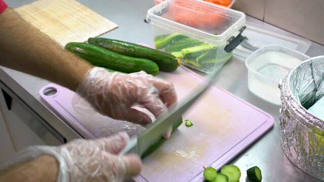 Close-up of a chef's hands cutting vegetables for traditional Asian cuisine with a knife. A professional sushi chef cuts a cucumber for rolls.