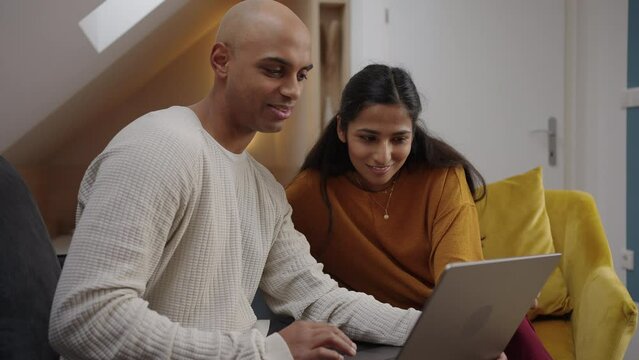 Two adults looking at a laptop and having relaxed conversation with someone over video meeting
