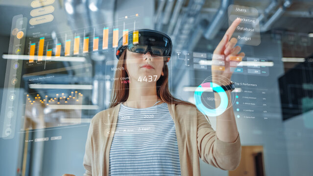 Young Adult Female Using Futuristic Augmented Reality Application Interface for Managing Business and Marketing Projects. Professional in Office Wearing Headset to Look at VFX Edit with Financial Data