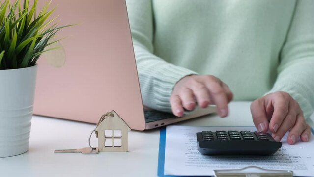 Woman calculating mortgage cost on calculator and entering data into laptop. Expenses on refinancing of home loan. Real estate investment concept