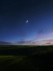 Crescent moon in the starry evening sky. Moon over green fields after sunset. Dreamlike night view.