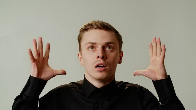 Young funny caucasian guy grimacing mind explosion on isolated on gray background. An emotional man in black shirt can't explain his experience. Unbelievable storytelling. Male amazed and surprised
