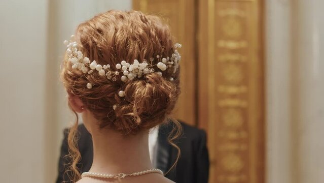 Rear view slowmo of unrecognizable red haired woman with elegant low bun and beaded headband standing in front of man asking her to dance at ball party in Regency ballroom