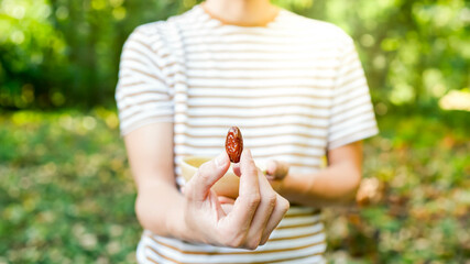 Closeup view of one date holded by unrecognizable white man in sriped tshirt with some other dates in a bowl behind it