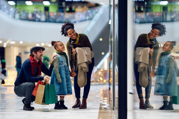 Happy parents with daughter looking at store windows at shopping mall.
