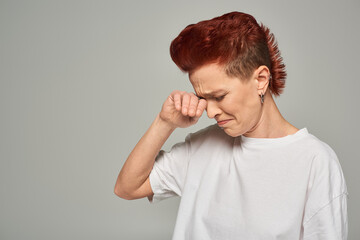 depressed and lonely bigender person crying and wiping tears on grey backdrop