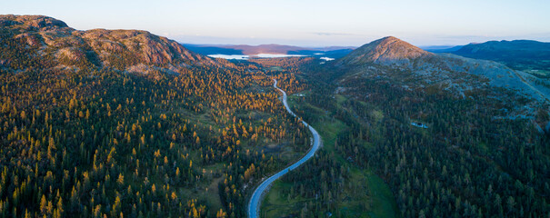 High angle aerial view of oad running through forest and mountainous landscape in northern Sweden