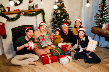 Obraz na płótnie Canvas Happy and cheerful Asian family gathering, wearing Santa hats talking and smiling. Exchanging gifts, grandparents, grandchildren, daughters, sitting at the fireplace with decorated Christmas tree.
