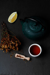 Hypericum Perforatum Herbal Tea In Teapot And small teacup and piace of lemon On Black Background....