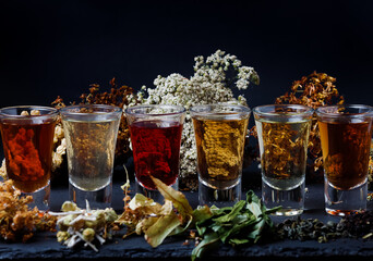 Assortment Herbal Tea in glass On Black Background. Low Key. Side view.