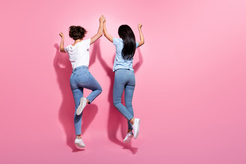 Full body size photo of active jumping two best friends hands together raise up trampoline rear...