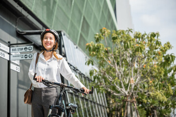 Morning motion and happiness An Asian businesswoman in a helmet and suit stands with her bicycle....