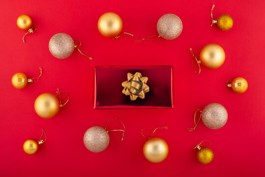 New Year concept. Top view photo of stylish giftbox with golden ribbon bow and Christmas decorations balls on isolated red background with copyspace.