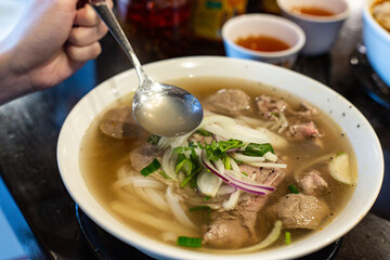 Classic Vietnamese Combination Beef Pho Topped with Freshly Onion and Coriander, with Spoon, Served in a Restaurant