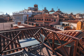 Balcony or terrace at a Venice apartment with a view of the city and rooftops. Table and chairs, peaceful atmosphere, no water visible. Architectural style and features not specified.