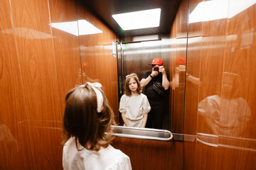 Happy father making photo of his daughter using professional camera in lift - obrazy, fototapety, plakaty