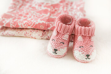 Pink knitted baby shoes near baby clothes on a white background with copy space. Congratulations on...
