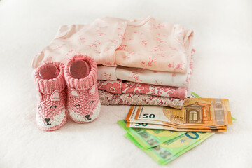 Clothes for a newborn, knitted socks for a baby and money on a white background. Pregnancy planning, motherhood. Family budget, children's money, child expenses