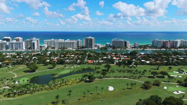 View from drone on popular La Gorce Club in Miami with green lawns, palm trees and water ponds. Modern residential buildings near Atlantic Ocean on background.