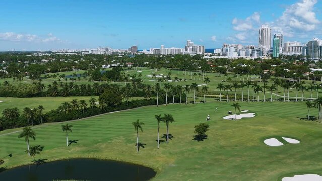 View from drone on La Gorce Club, large green area with palm trees and luxury residential complexes in distance. Magnificent place for playing golf under bright summer sun