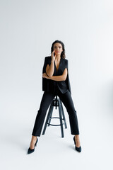 Fototapeta premium A luxurious sexy and beautiful girl at a photo shoot in a photo studio poses stylishly and fashionably in a black trouser suit