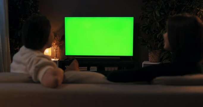 Green screen mockup tv. Over the shoulder shot two women friends sitting in the living room watching tv films movie news talking spending time together resting after hard day at work weekend time.