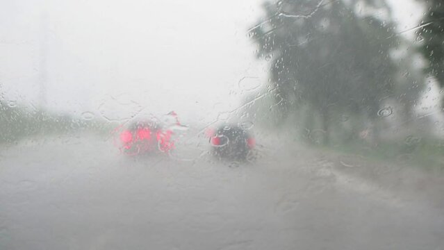 View through running car windshield during heavy rain. Wiper is cleaning the windshield glass. Traffic on highway during heavy rain in rainy season.