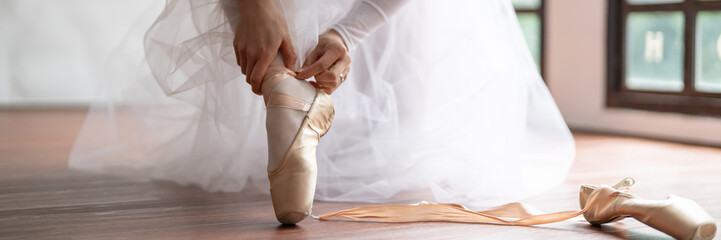 Ballerina in ballet shoes. Asian girl tying ribbons of toe shoes. ballet dancer preparing and wearing ballet shoes in dance studio prepares for a rehearsal.