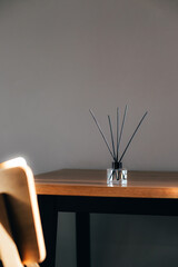 Aroma diffuser in a clear glass bottle with black cap on wooden table on a strip of sunlight. Front...