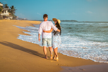 Happy couple walking on tropical beach at sunset