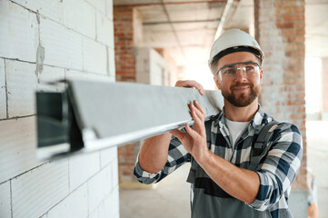 Holding metal plank. Construction worker in uniform in empty unfinished room