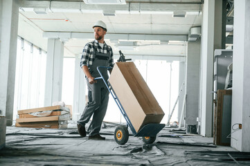 Transporting long paper box. Construction worker in uniform in empty unfinished room