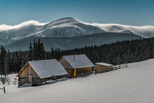 Two wooden log cabins under moonlight in winter Carpathian mountains