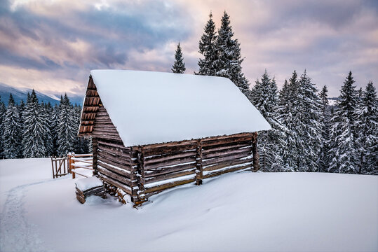 Wooden log cabin hut in snowy mountains under cloudy sky