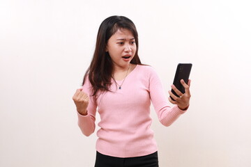 Fototapeta premium Unhappy angry young asian girl standing while holding a cell phone. Isolated on white background
