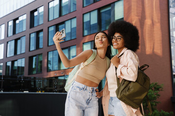 Two smiling female friends students taking selfies while standing in university campus