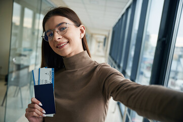 Smiling, holding tickets. Young woman traveler in the airport entrance hall