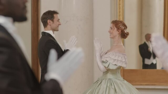 Medium shot of delighted multiracial couples in aristocratic outfits hand dancing at ball party during ceremonial reception
