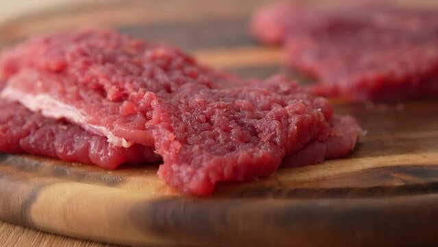 Panning shot of the process of beating raw meat on a wooden board.